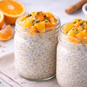 Vegane Overnight Oats mit Zitrusfrüchten im Glas, garniert mit Orangenstücken, Mandarinen und Nüssen auf hellem Hintergrund