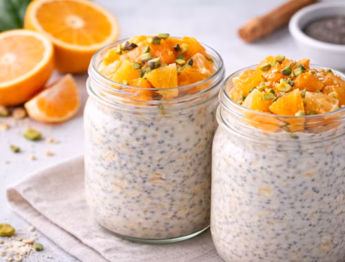 Vegane Overnight Oats mit Zitrusfrüchten im Glas, garniert mit Orangenstücken, Mandarinen und Nüssen auf hellem Hintergrund