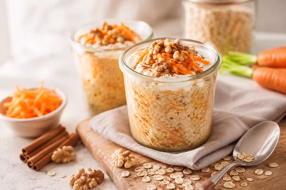 Carrot Cake Overnight Oats im Glas mit Karotte, Hafer, Zimt und Walnüssen auf hellem Frühstückstisch