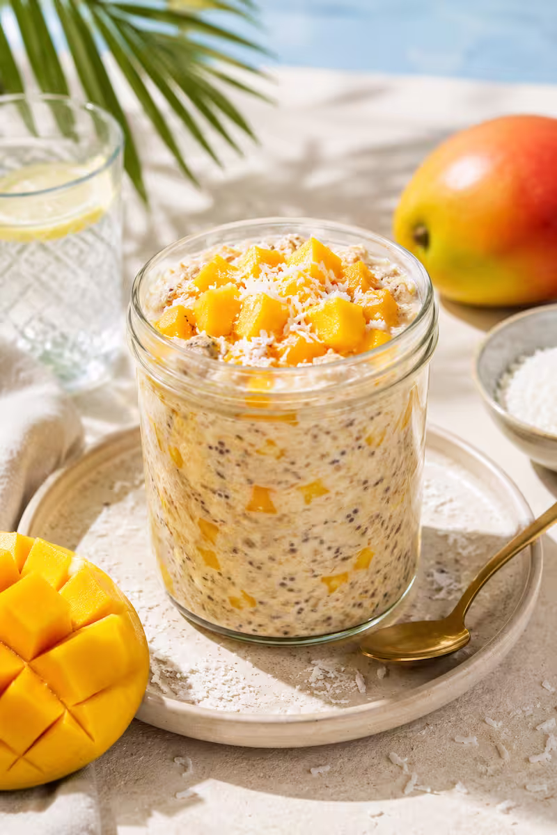 Mango Overnight Oats im Glas Mango Overnight Oats im Glas mit Kokosraspeln und frischen Mangowürfeln auf hellem Sommertisch