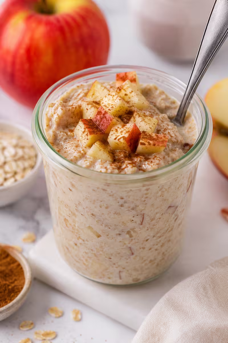 Nahaufnahme Overnight Oats mit Apfelwürfeln Nahaufnahme cremiger Overnight Oats mit Apfelwürfeln, Zimt und Löffel im Glas