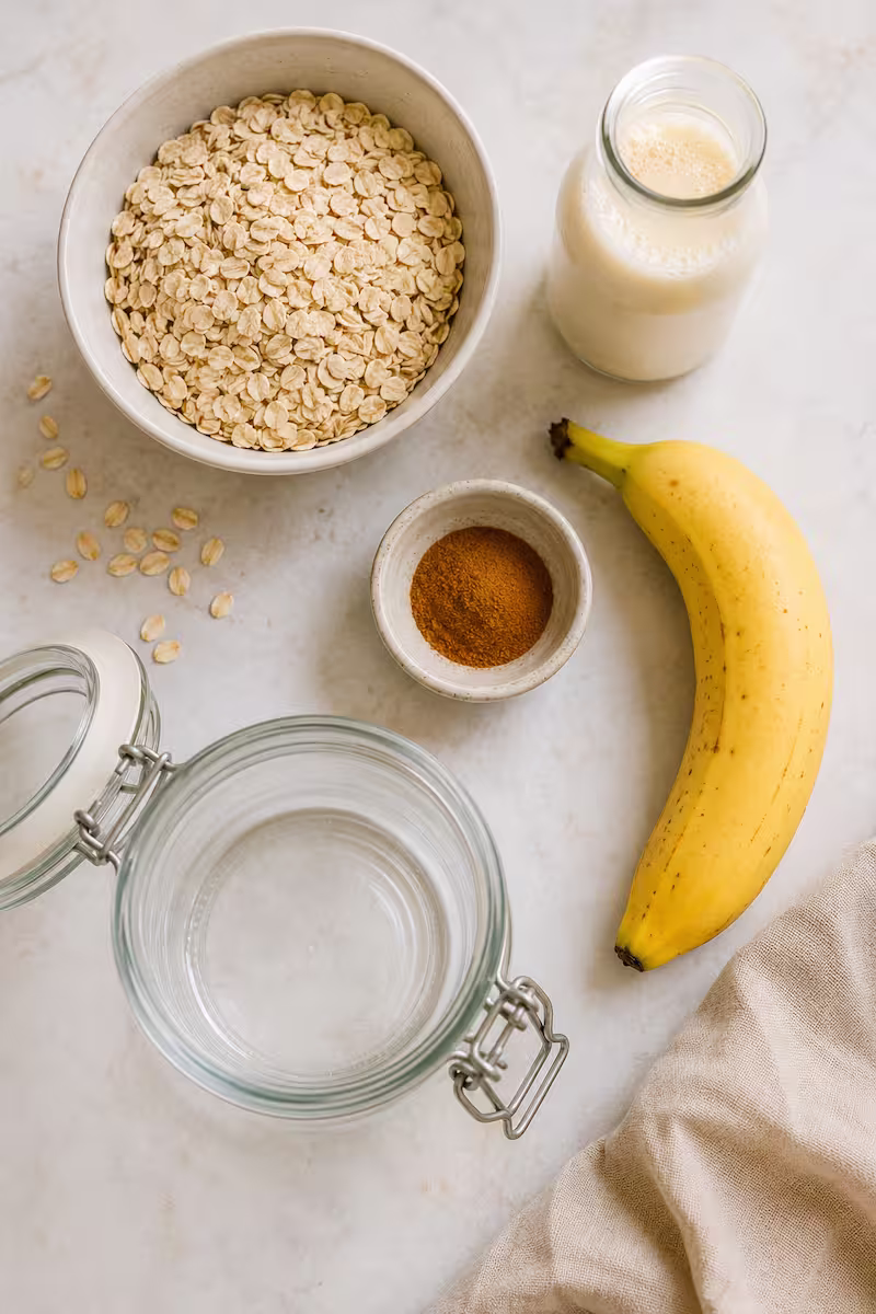Zutaten für Overnight Oats Banane Zutaten für Overnight Oats Banane von oben fotografiert, Haferflocken, Banane, Hafermilch, Zimt und Glas auf hellem Untergrund