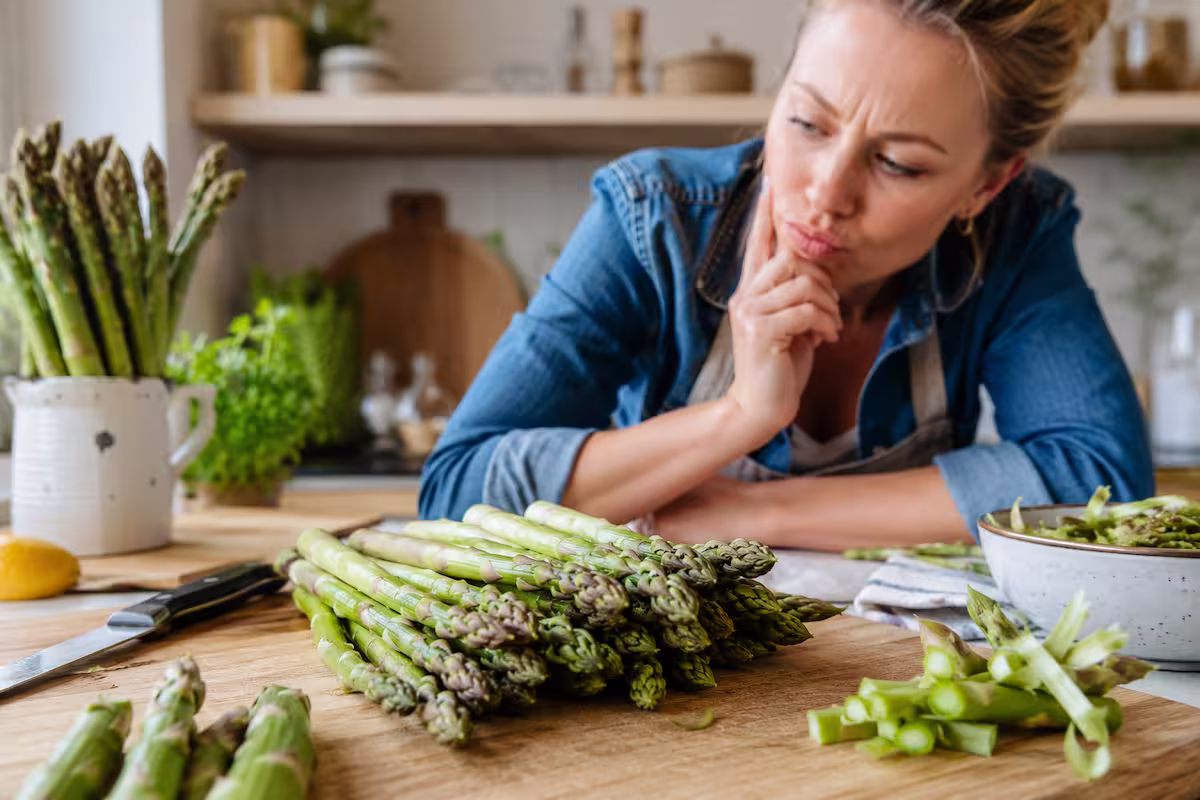 Frau in heller Küche betrachtet frischen grünen Spargel auf einem Holzbrett und vermeidet typische Fehler bei der Zubereitung – Grüner Spargel: Die häufigsten Fehler vermeiden